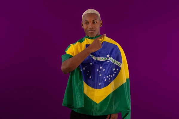 Brezilya bayrağını tutan siyah tenli bir adam ve stüdyo fotoğrafında Brezilya futbol takımının gömleğini giyiyor.