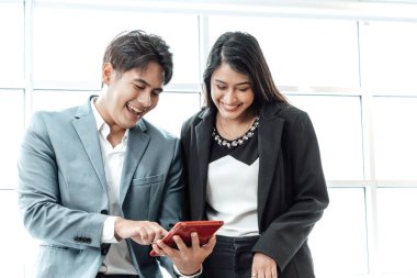 Mutlu iş çifti birlikte durup pencere arkaplanının yakınındaki tablet üzerindeki çalışmaları kontrol ediyor.