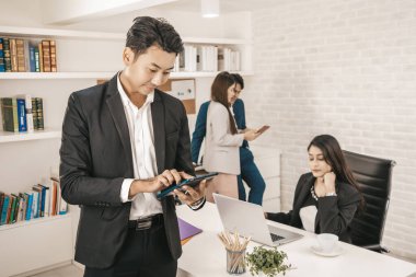 Yakışıklı bir CEO 'nun portresi, pozitif görünüşlü genç bir iş adamının portresi arka planda iş arkadaşlarıyla konuşurken tablet kullanması..