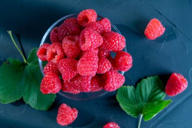 Koyu arkaplanda kırmızı ahududu olan bir cam kase..