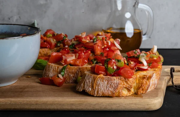 이탈리아 토마토 브루 체타를 나무 도마 위에 얹고 마늘을 곁들인 토마토, 향신료, 바질을 곁들인 그릇을 놓는다 — 스톡 사진
