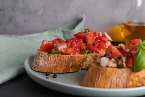 Duas fatias de bruschetta de tomate feito de pão ciabatta com tomates em cubos, especiarias, manjericão e alho picado em um prato, cozinha italiana, foco seletivo — Fotografia de Stock