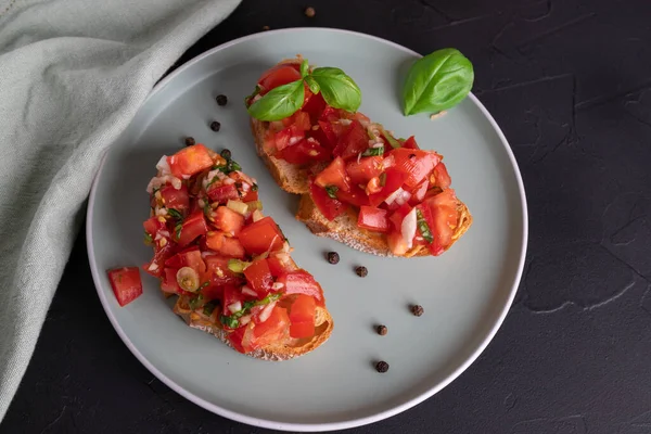 Duas fatias de bruschetta de tomate feitas de pão ciabatta com tomate em cubos, especiarias, manjericão e alho picado em um prato, cozinha italiana, vista superior — Fotografia de Stock