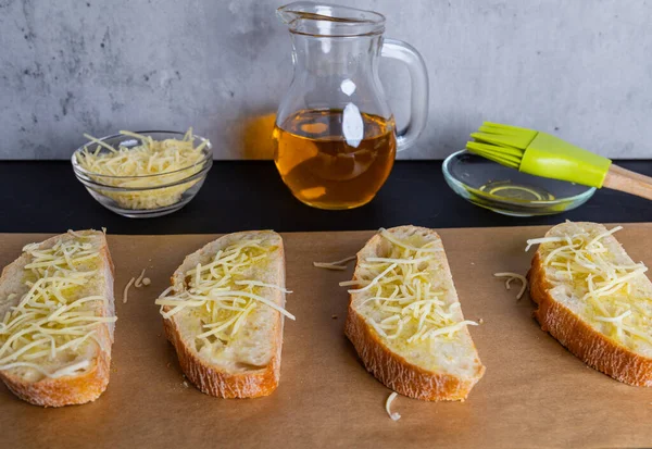 Irisan ciabatta renyah dilapisi dengan minyak zaitun dan ditaburi dengan keju parut, siap dipanggang dalam oven untuk bruschetta — Stok Foto