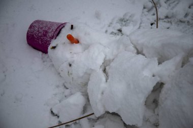 Düşmüş kardan adam bahçede karların üzerinde yatıyor.