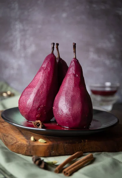 Pears in red wine on a ceramic plate and concrete wall background, still life concept, vertical view, close up