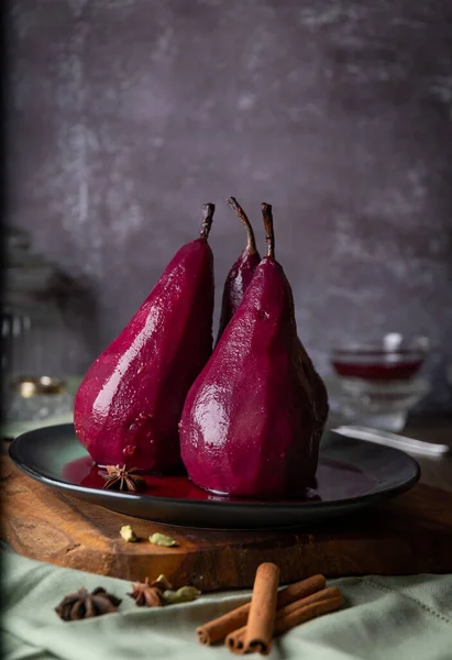 Pears in red wine on a ceramic plate and concrete wall background, still life concept, vertical view, copy space