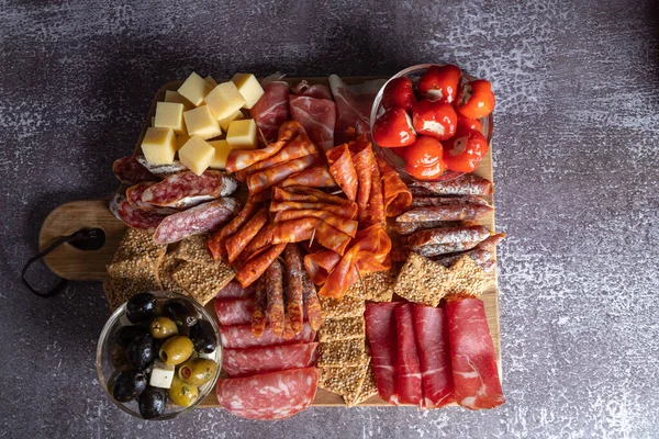 Tábua de corte com presunto, salame, queijo, bolacha e azeitonas em uma tábua de madeira. — Fotografia de Stock