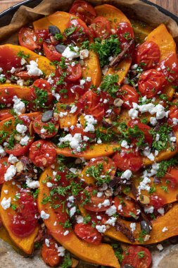 Lezzetli Hokkaido balkabağı körili, mini domatesli, fındıklı, kabak tohumlu, hurma ve koyun peynirli, koyu kırsal bir zeminde pişirilmiş..