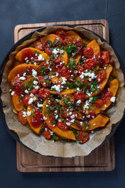 Lezzetli Hokkaido balkabağı körili, mini domatesli, fındıklı, kabak tohumlu, hurma ve koyun peynirli, koyu kırsal bir zeminde pişirilmiş..