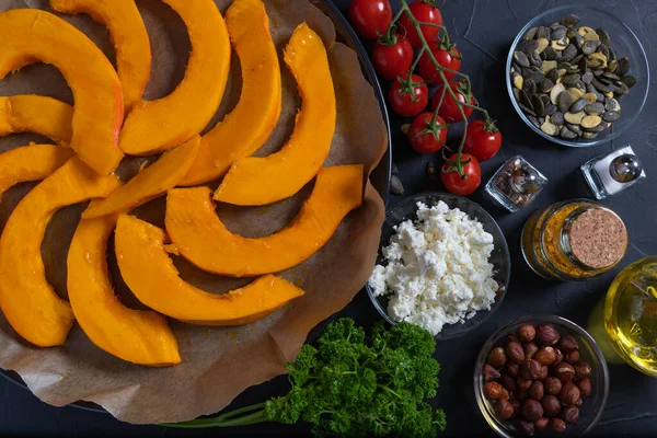 Köriyle dilimlenmiş Hokkaido kabağı, mini domates, fındık, kabak tohumu, hurma ve beyaz peynir, graten için hazırlanmış koyu kırsal bir zemin..