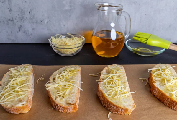 Irisan ciabatta renyah dilapisi dengan minyak zaitun dan ditaburi dengan keju parut, siap dipanggang dalam oven untuk bruschetta — Stok Foto