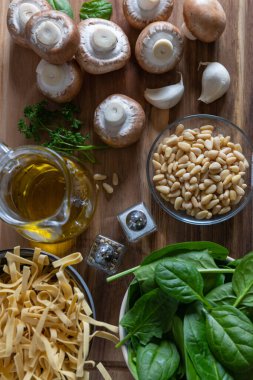 Rustik Mantar Ispanak Makarnası 'nın malzemeleri. Mantar, ıspanak, sarımsak karanfil, çam fıstığı, baharat, zeytinyağı ve maydanoz ahşap arka planda, üst manzara.