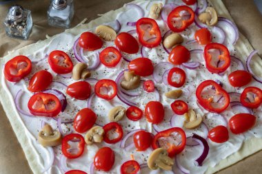 Turta pişirmeye hazır ve krema hamurunda dilimlenmiş soğan, domates ve mantarla kaplanmış..