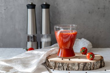 Gri arkaplanda domates suyu, biber, tuz ve domatesli bardak..