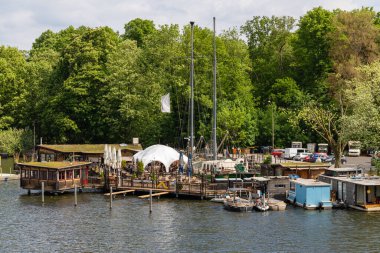 Berlin-Treptow, Almanya - 21 Mayıs 2022, Kulturinsel, Insel der Jugend karşısındaki Treptower Park 'ta restoranları ve birkaç tekne kiralama ile Spree manzarası. Gezi tekneleri nehirde yüzüyor..