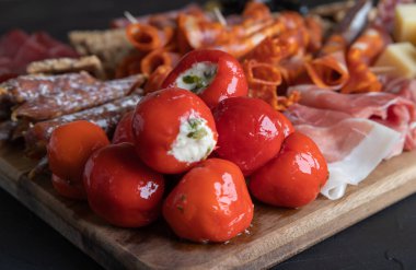 Koyu arkaplanda jambon, salam, peynir, kraker ve zeytin kesme tahtası. Peynirle doldurulmuş kırmızı biber yakın plan..