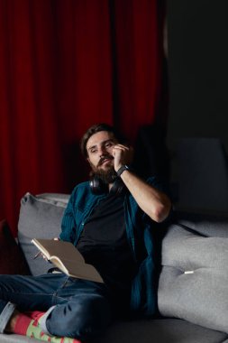 Hippi, not defterine not tutarken içeride sesli kitap dinlemeye ara veriyor. Oturma odasındaki kanepesinde oturuyor..