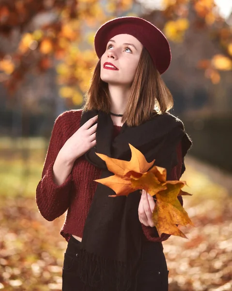 Autumn portrait of beautiful brunette in red sweater , holding yellow leaves, looking in the distance