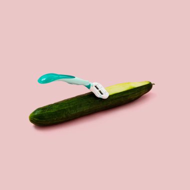 Green large cucumber with a razor blade on a pastel pink background. The concept of depilation care. Abstract poster.
