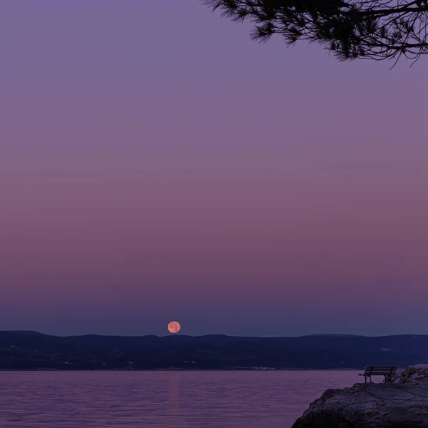 A beautiful view of the setting moon and the island at dawn on the coast of the Adriatic Sea in Croatia. Concept summer vacation.