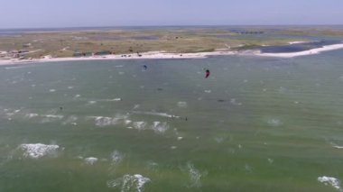 Yazın güneşli bir günde Karadeniz sahilinde rüzgar sörfü yapan iki sporcunun paraşüt altında Karadeniz kıyısında kumlu kıyılarda ve yazın parlayan dalgalarla rüzgar sörfü yapmasını gösteren hava görüntüleri..