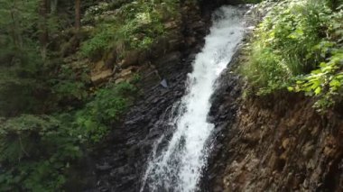 Yazın güneşli bir günde, sarp yeşil bir dağdan akan canlı şelale, güneşli bir yaz gününde Karpat dağlarındaki sarp kayalıklardan akan aktif bir şelalenin etkileyici manzarası. Neşeli ve güzel görünüyor..