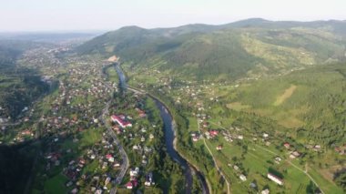 Yazın modern otoyolu ve nehri olan yeşil bir dağ sırtı ve vadisinin havası. Yeşil yamaçlı muhteşem bir dağ tepesi, parlak bir nehir, yüksek köknar ağaçları, şeritler, evler ve güneşli bir günde hareket eden arabalarla dolu bir otoyol.