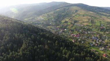 Yaz mevsiminde aralarında evler olan bir dağ sırtının havadan çekilmiş görüntüsü. Güneşli bir yaz gününde aralarında iki tepe ve bir vadi ile küçük evler, şeritler ve çayırlarla kaplı bir dağ sırtı manzarası..
