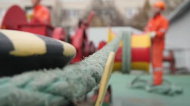 Sağlam bir naylon askısı var. Yoncadan çalı çırpı olan bir işçiye dönüşüyor. Orijinal Bokeh yakın plan sert naylon bir çekici döner ve metalik bir kazıktan sonbaharda bir atölyede büyük metalik bir rüzgar kıçı olan bir adama gider..