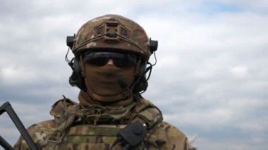 Bulutlu bir günde, üniformalı, gözlüklü ve miğferli modern bir asker. Üniformalı, siyah gözlüklü, miğferli ve maskeli çağdaş bir asker baharda bulutlu bir günde tarlada dikilip ileriye bakıyor.