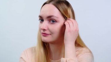 Stüdyoda gülümseyen ve saçlarını beyaz arka planda düzleştiren genç sarışın kadını kapatın. Yüksek kalite 4k görüntü