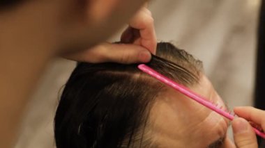 Berber, pembe tarak kullanan gri saçlı yaşlı bir adamın ıslak saçlarını ayırıyor. Yüksek kalite 4k görüntü