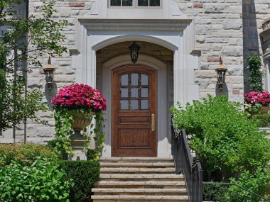 Zarif ahşap ön kapısı ve dekoratif saksıları olan taş bir ev.