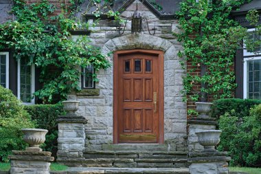 Çiçek saksıları ve sarmaşıklı taş evin zarif ahşap ön kapısı.