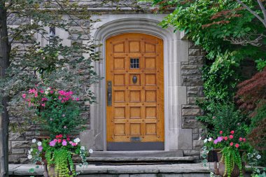 Taş evin zarif ahşap ön kapısı yaz çiçekleri ve ağaçlarla çevrili.