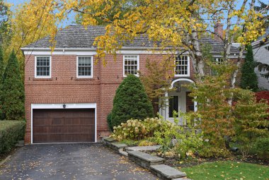 Çifte garaj yolu olan tuğladan bir ev ve ağaçların üzerine düşen yapraklar.