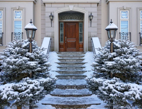 Kışın evin ön kapısında karla kaplı çam çalıları olan zarif ahşap kapılar.