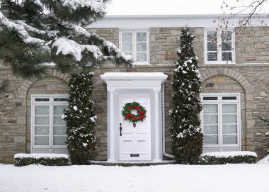 Ön kapısında parlak süslenmiş Noel çelengi olan geleneksel evin önünde.