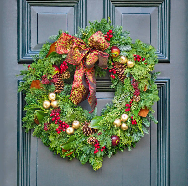 Входная дверь с рождественским венком из сосновых ветвей, шишек, красных ягод и золотых яблок