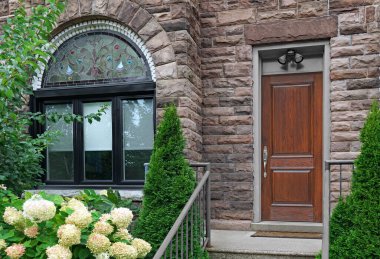 Beyaz ortancalar ve ardıç çalıları olan eski taş evin ahşap ön kapısı.