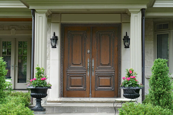Elegant portico entrance with wood grain double door surrounded by flowers and bushes