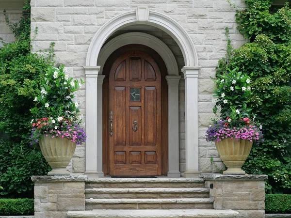 丸みを帯びた前庭の石造りの家のエレガントな木目のフロントドア ブドウや花に囲まれて ストックフォト