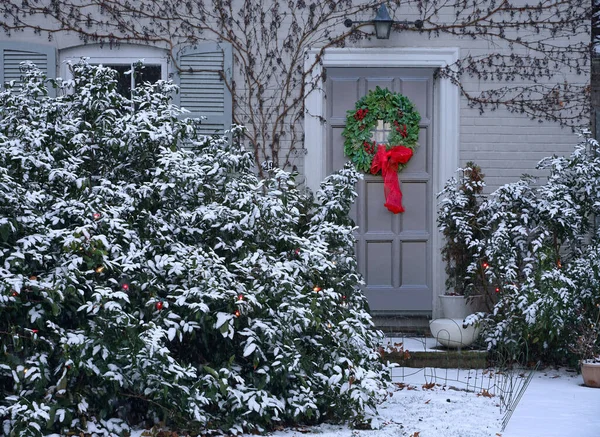 Traditional house with snow covered bushes and Christmas decoration wreath on the front door