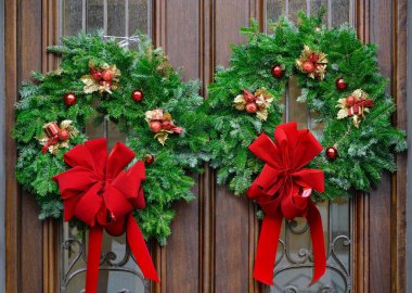 Kırmızı kurdeleli çam dalından yapılmış çelenklerle ahşap çift ön kapı.