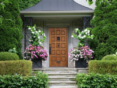 Çiçekler ve çalılarla çevrili zarif ahşap ön kapı.