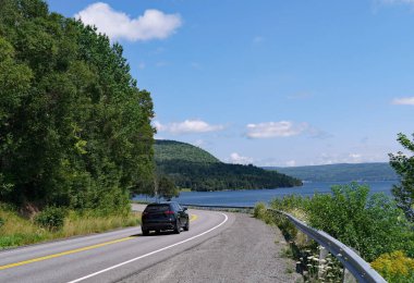 Car driving on a scenic highway beside a lake clipart