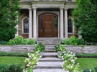 Elegant wood grain front door of house on porch with columns surrounded by shrubbery