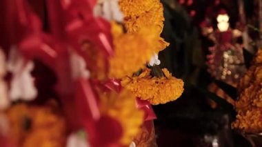 Close up marigold wreath flowers in Asian temple, orange colors with red ribbons and some other flowers dark temple with some statues in the background, slow motion, High quality FullHD footage