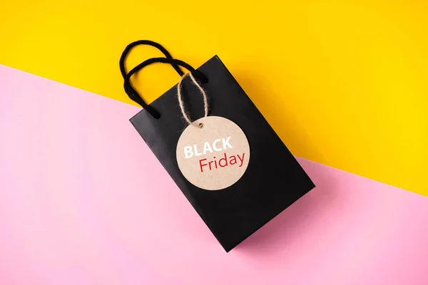 Black gift bag with label on colored background black friday concept.